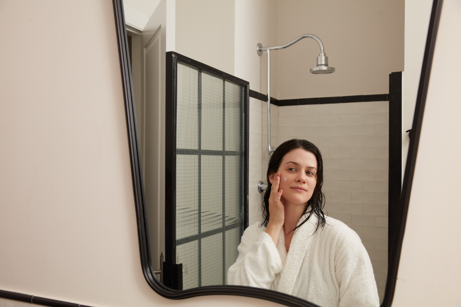 Kobieta oddająca się pielęgnacji cery przed luistrem po wzięciu prysznica